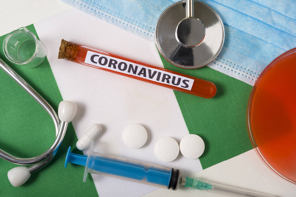 Coronavirus, nCoV έννοια. Προστατευτική μάσκα αναπνοής, στηθοσκόπιο, σύριγγα, δισκία στη σημαία της Νιγηρίας. Ένα νέο ξέσπασμα του κινεζικού coronavirus - Φωτογραφία, εικόνα