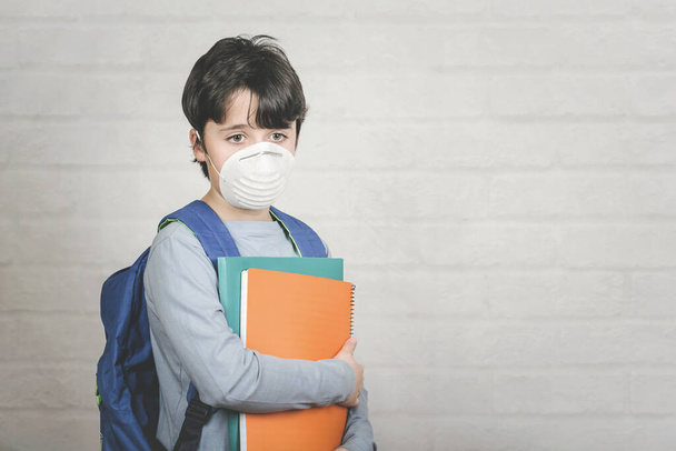 Coronavirus.Sad child with medical mask and maskbackpack over brick background - Photo, Image
