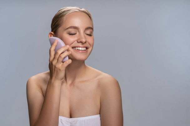 Positive delighted blonde girl cleaning her face - Foto, afbeelding