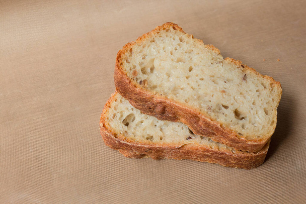 Σπιτικό ψωμί σίκαλης χωρίς μαγιά από ζωντανό προζύμι. Δύο φέτες ψωμιού σίκαλης με λιναρόσπορο και ηλιόσπορους σε ένα μπεζ λινό τραπεζομάντηλο από τον χώρο της Κοπής - Φωτογραφία, εικόνα