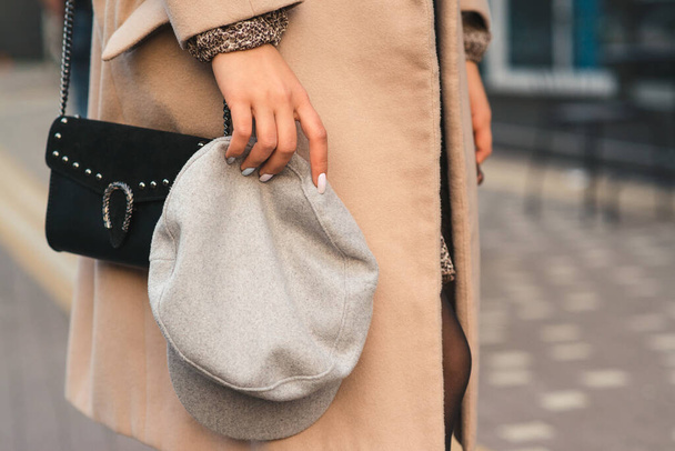 Woman holding cap, close up. Young woman with black handbag. Spring and autumn fashion. Grey trendy hat cap. Women fashion, street style. Fashionable stylish look in pastel colors. Stylish woman. - Φωτογραφία, εικόνα