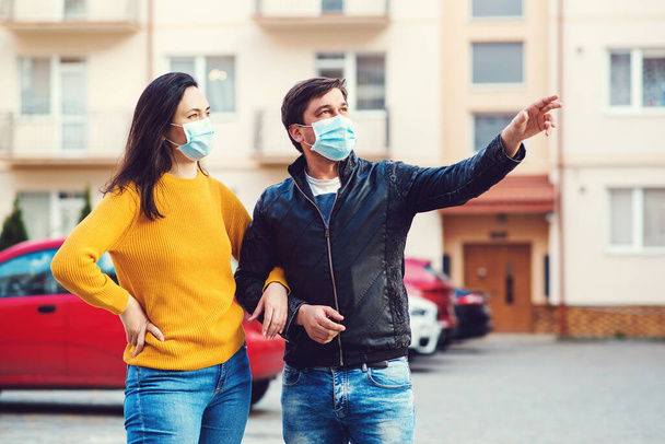 若いカップルは屋外で医療マスクを着用。2020年春の生活。コロナウイルスの流行。コロナウイルスの拡散防止。肯定的な感情を持つ顔のマスクの人々。世界的なコロナウイルスのパンデミック. - 写真・画像