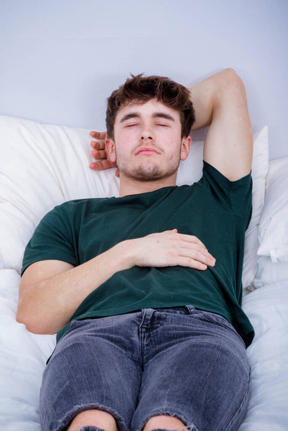 A young adult man laying on his back sleeping in his clothes on a bed - Foto, Imagen