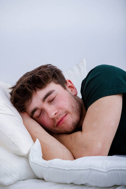 Een jonge volwassen man slaapt in zijn kleren op een bed - Foto, afbeelding