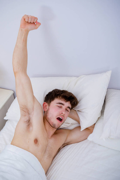 Egy fiatal felnőtt férfi reggel felébred és nyújtózkodik. - Fotó, kép