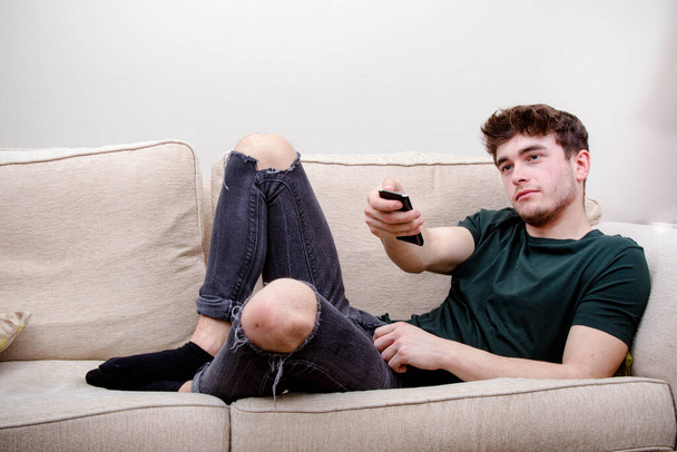A young adult man using a remote control while on a sofa - Foto, immagini