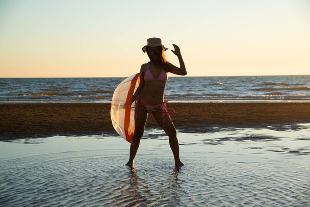 Silhoutte of a pretty senior Asian female in a swimming suit standing and hold umbrella posing on the beach.  - Fotó, kép