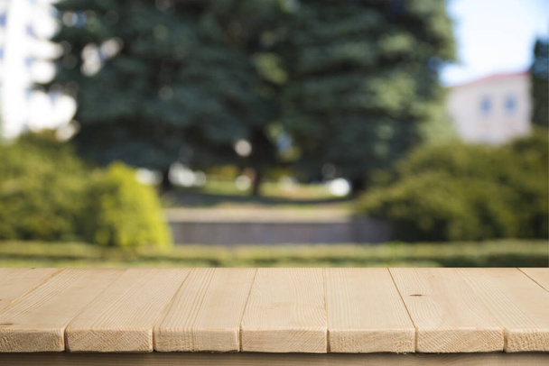 Empty wooden deck table with foliage bokeh background. Ready for product display montage. - Photo, Image