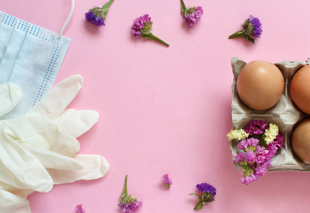 Kesztyű, arcpakolás, virágok és tojások világos rózsaszín háttér felülnézet. Húsvét a koronavírus koncepció alatt. - Fotó, kép