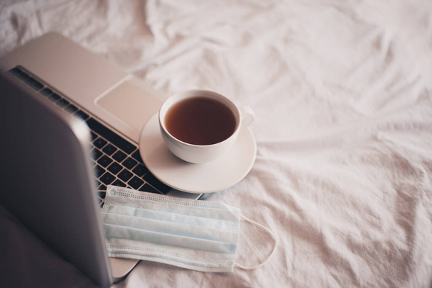 Egy csésze tea arcpakolással, nyitott laptopon az ágy közelében. - Jó reggelt! Reggeli. Társadalmi távolság. Karantén ideje.  - Fotó, kép