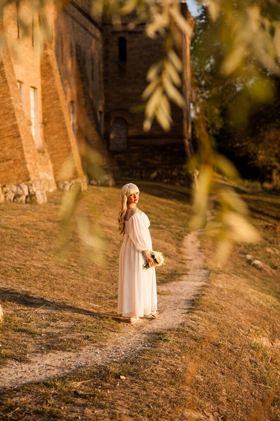 blondi tyttö valkoinen mekko luontoon lähellä arkkitehtonisia monumentteja ulkona
 - Valokuva, kuva