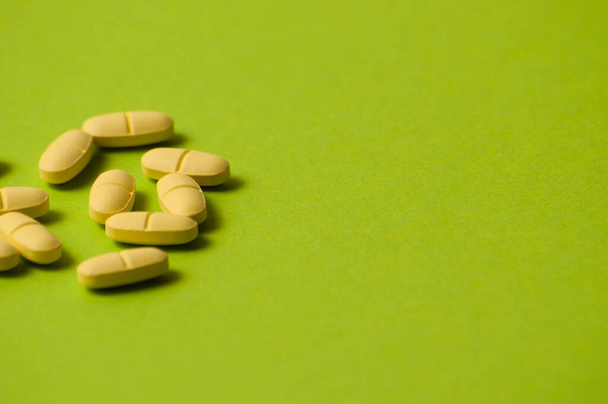 Many yellow pills on green background with room for copy space - Foto, afbeelding