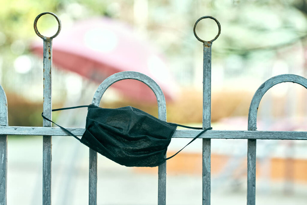 μαύρη ιατρική μάσκα κρεμασμένη στον φράχτη ενός άδειου νηπιαγωγείου. Καραντίνα. κοβίδιο-19 - Φωτογραφία, εικόνα