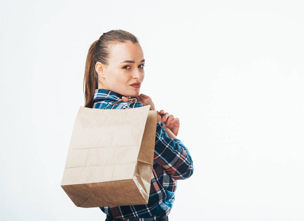 Woman is holding grocery shopping bag on white background. Young girl is holding light brown shopping bag behind back. Isolated background. Look from the back. Closeup. - Zdjęcie, obraz