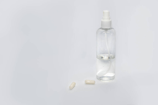 Spray trigger, witte plastic pulverizer op witte achtergrond met capsules pillen. Ontsmetten spray cosmetica trekker. Aerosol transparante fles close-up. Verzorger voor schone verzorging - Foto, afbeelding