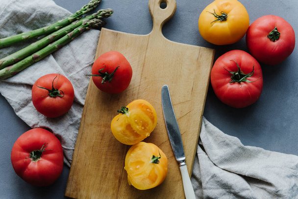 Pomidor w żółtym plasterku na desce do krojenia w pobliżu czerwonych i żółtych pomidorów. - Zdjęcie, obraz