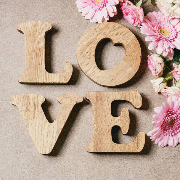 Word LOVE from oak wooden letters with variety of pink roses flowers over brown texture background. Flat lay, space. St. Valentines greeting card - Фото, изображение