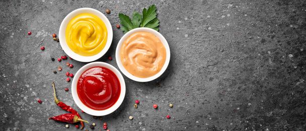 Top view of yellow mustard, red ketchup and paprika sauce in small bowls on gray concrete background with copy space - Foto, immagini