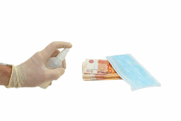 A hand in a white glove handles five thousand 5000 rubles, next to a blue medical mask, with an antiseptic. The concept of virus protection is the use of precautions when shopping in stores in Russia. Isolated white background. - Photo, image
