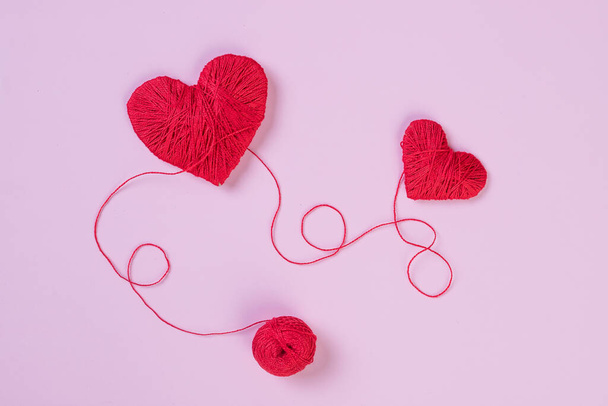 Warmes Wollherz, Symbol der Liebe, aus roten Wollfäden, isoliert über rosa Hintergrund. red thread.heartbeat.Holiday Konzept, Zwei Herzen. - Foto, Bild
