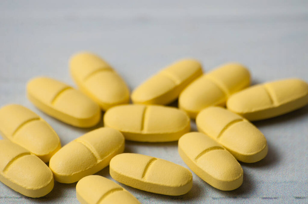 Spousta žlutých pilulek zblízka makro na lehkém dřevěném stole. - Fotografie, Obrázek