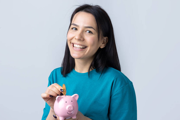 Das Mädchen hält ein rosafarbenes Sparschwein und eine Münze in der Hand. Das Konzept von Reichtum und Akkumulation. - Foto, Bild