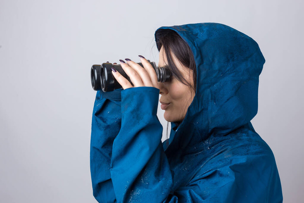 Туристична дівчина в синьому плащі тримає бінокль в руках і дивиться на відстань, шпигуни
. - Фото, зображення