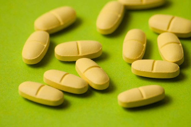 Muchas píldoras, antibióticos o vitaminas de color amarillo sobre fondo verde primer plano, primer plano
 - Foto, Imagen