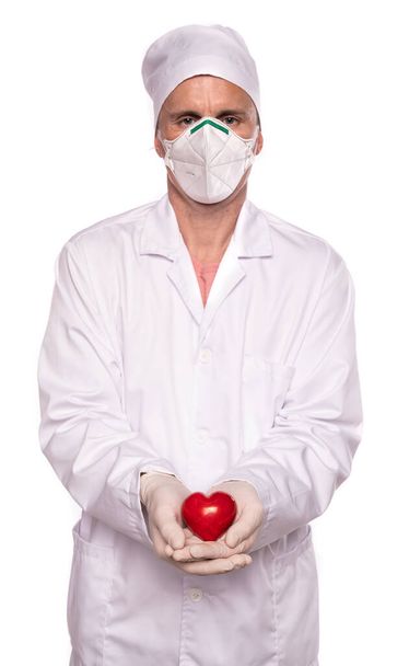 Healthcare and medical concept. Male doctor in gloves and mask holding heart over white background - Foto, Bild