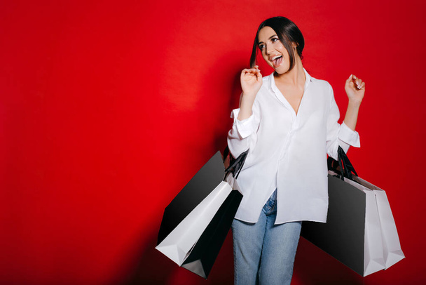 Excited woman with lots of shopping bags dancing isolated on a red background. - Foto, immagini