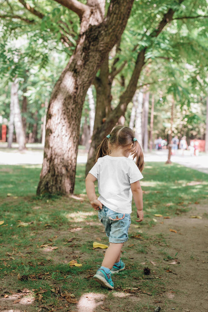 back views of little girl in blank t-shirt walking in park. Mockup for design - 写真・画像