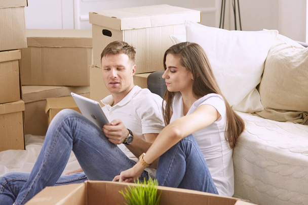 Portrait de couple heureux regardant ordinateur portable ensemble assis dans une nouvelle maison, entouré de boîtes
 - Photo, image