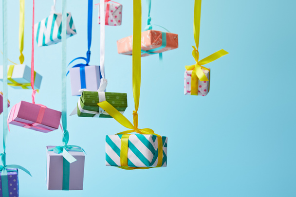 festlich bunte Geschenkboxen hängen an Bändern auf blauem Hintergrund - Foto, Bild