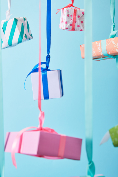 selectieve focus van feestelijke kleurrijke geschenkdozen opknoping op linten geïsoleerd op blauw - Foto, afbeelding