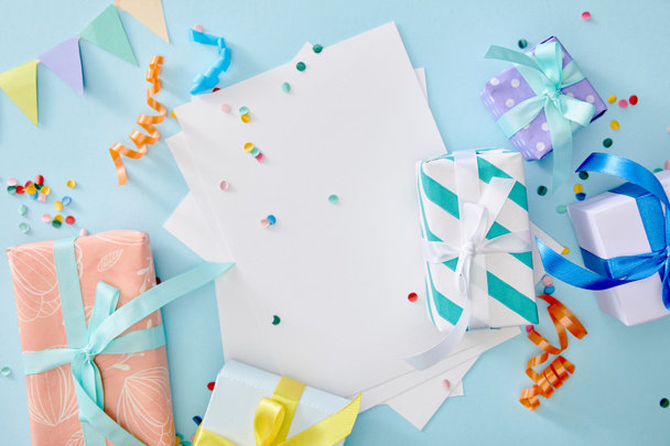 top view of colorful confetti near blank paper and gift boxes on blue background - Fotografie, Obrázek