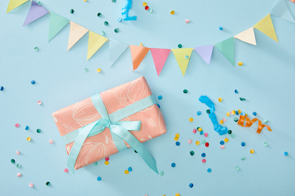 top view of colorful confetti near gift box on blue background - Foto, Imagem