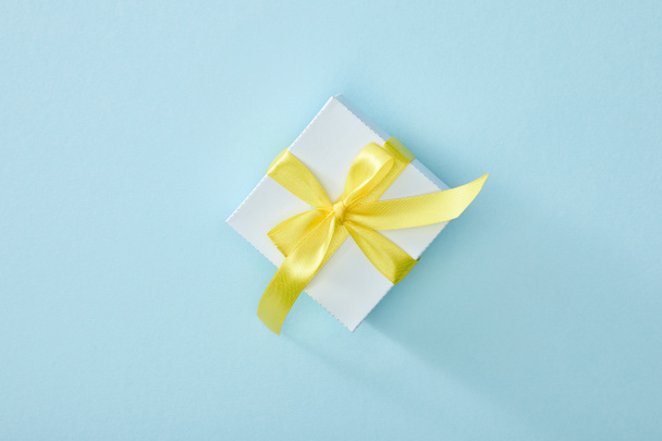 top view of festive gift box with yellow ribbon on blue background - Foto, immagini