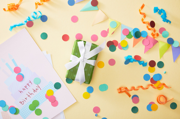 top view of festive colorful confetti and gift with happy birthday greeting card on beige background - Фото, зображення