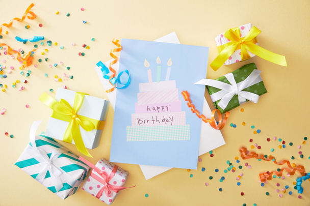 vista superior de confeti colorido festivo, regalos y feliz cumpleaños tarjeta de felicitación sobre fondo beige
 - Foto, Imagen