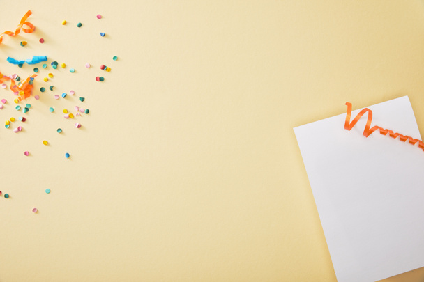 top view of festive colorful confetti near blank paper on beige background - Foto, imagen