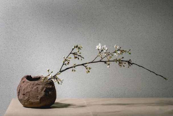 Blossom cherry branches in craft clay vase on grey table cloth. Spring interior decorations. - Foto, Bild