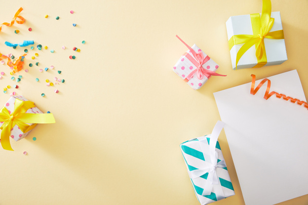 top view of festive colorful confetti and presents near blank paper on beige background - 写真・画像