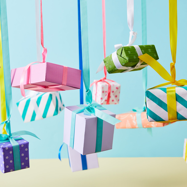 festlich bunte Geschenkboxen hängen an Bändern auf blauem Hintergrund - Foto, Bild