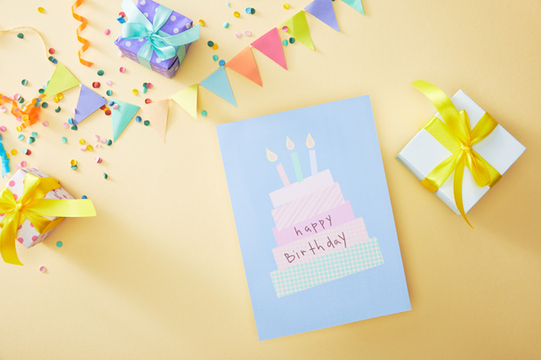 top view of festive colorful confetti and gift boxes near happy birthday greeting card on beige background - Photo, Image