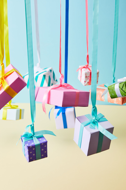 cajas de regalo de colores festivos colgando de cintas sobre fondo azul y amarillo
 - Foto, imagen