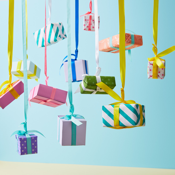 boîtes cadeaux colorées festives suspendues sur des rubans sur fond bleu
 - Photo, image