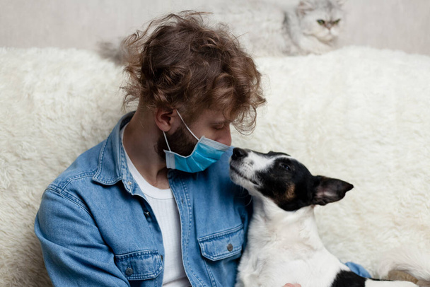Un hombre con su mascota está sentado en un sofá en casa. Coronavirus cuarentena
. - Foto, imagen