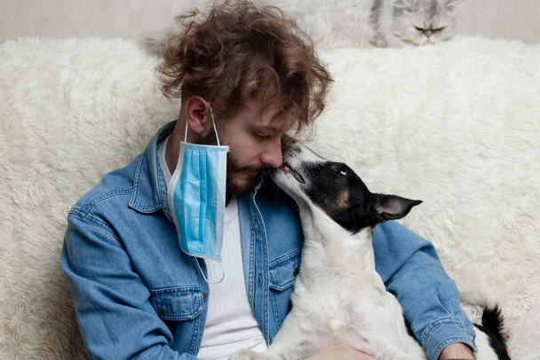 Een man met zijn huisdier zit thuis op een bank. Quarantaine-coronavirus. - Foto, afbeelding