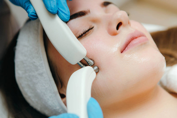 Close-up foto van een vrouw met een stimulerende gezichtsbehandeling van een therapeut. Micro-stroomtherapie. - Foto, afbeelding