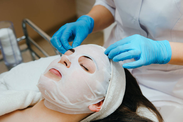 Face peeling mask, spa beauty treatment, skincare. Woman getting facial care by beautician at spa salon. - Photo, Image